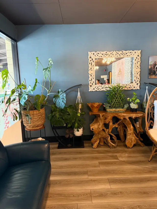 Tranquility Spa lounge: a teak-root console, a carved white mirror, monstera and potted plants against a blue wall