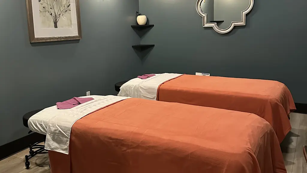 Treatment room with two massage tables dressed in terracotta throws against slate-teal walls under pendant spotlights